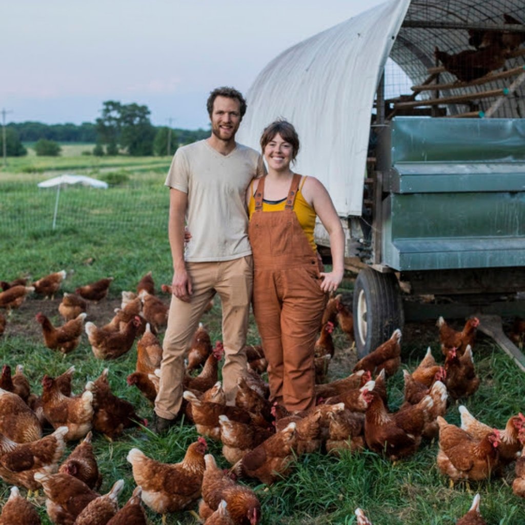 Timberfeast Farmers Mark Brady and Katie Kennedy standing next to their portable chicken coop with pasture-raised chickens at their feet. 